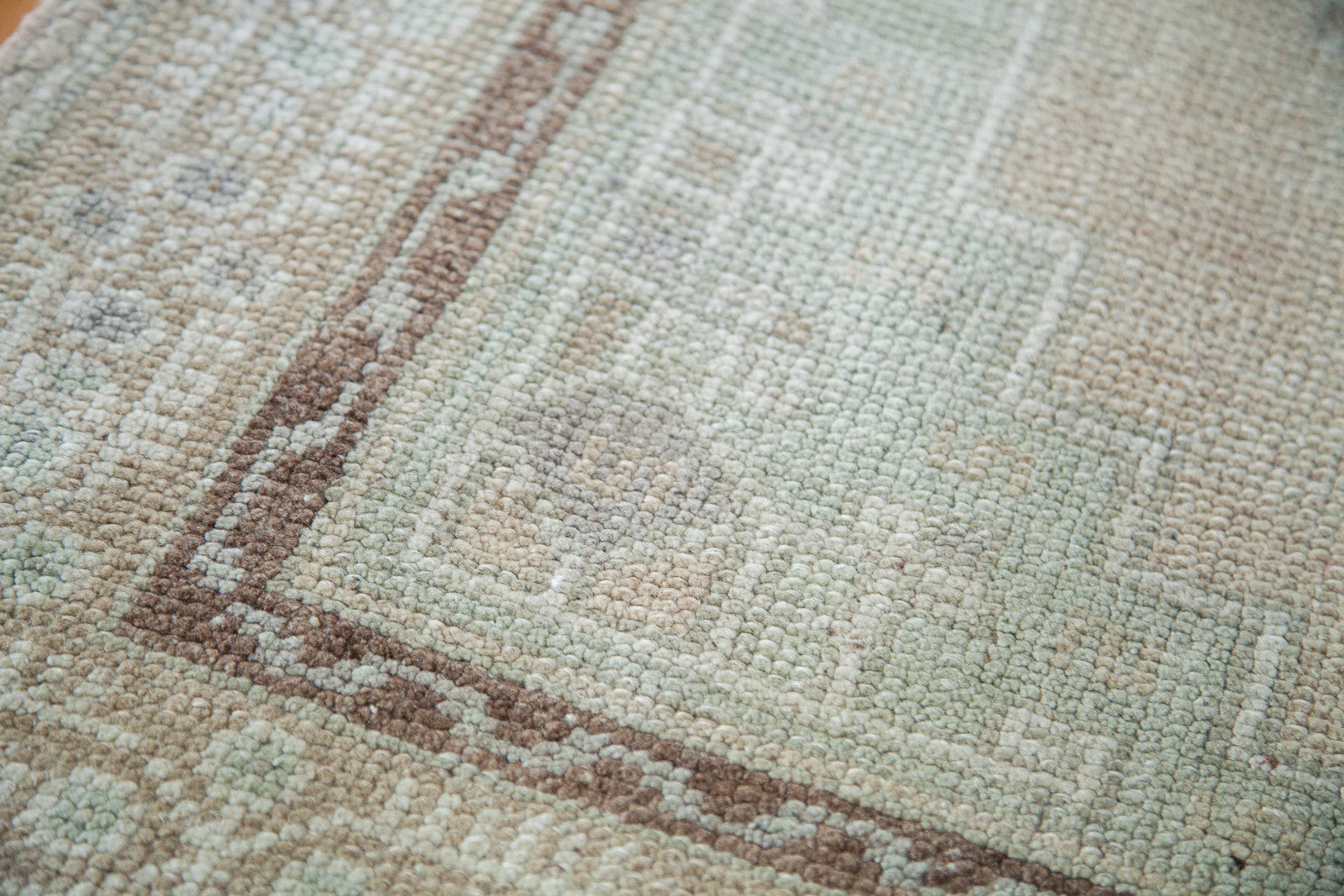 Corner of Vintage Oushak rug with contrasted brown border and peach, mint green.